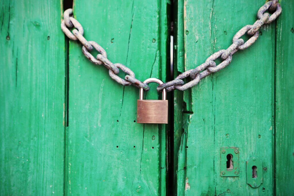 A rusty chain and padlock secure a weathered green wooden door, with visible wear and a keyhole nearby.