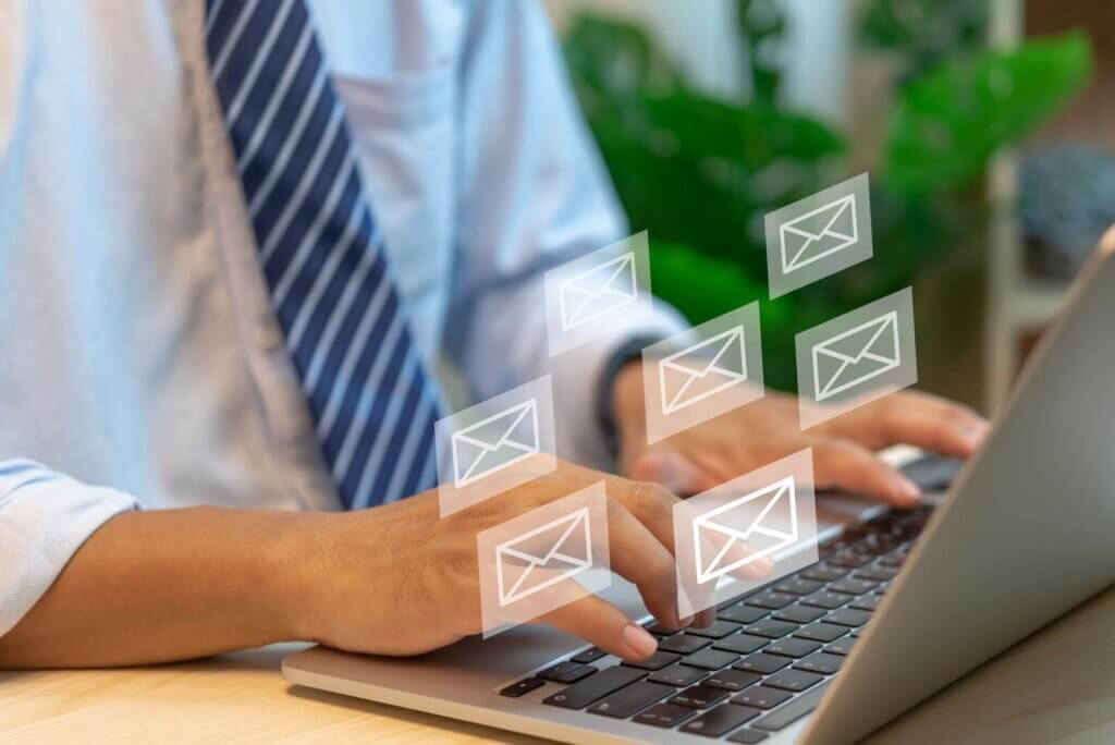 Person typing on a laptop with email icons floating above, symbolizing digital communication.