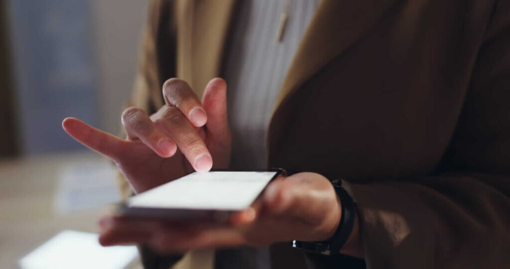 A person in a brown jacket uses a smartphone, tapping the screen with their index finger.