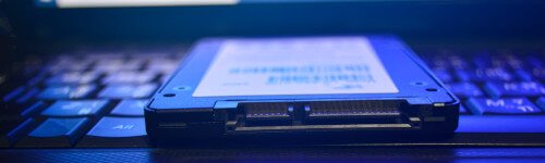 A solid-state drive (SSD) rests on a laptop keyboard, illuminated by a blue light.