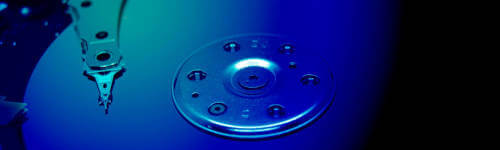 Close-up of a hard disk drive platter and read/write head, illuminated in blue light.